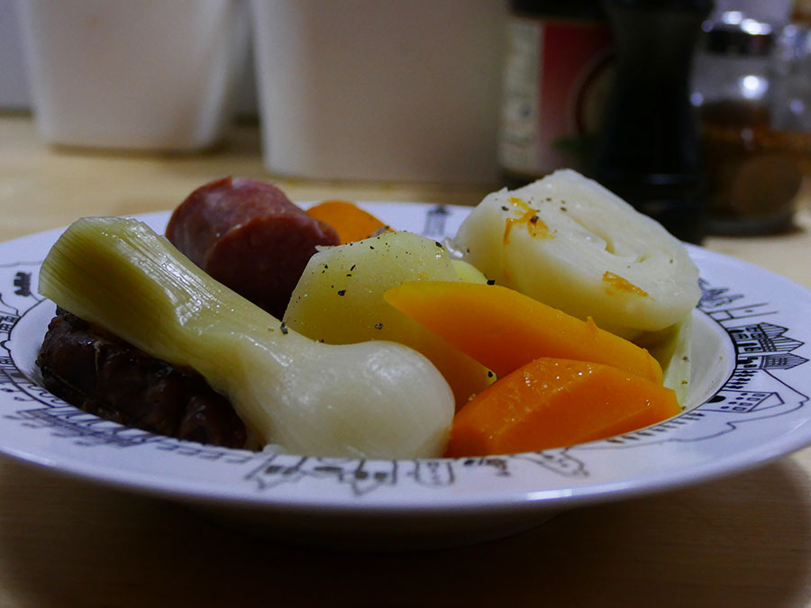 recette de la potée une vrie recette d'hiver avec des carottes multicolores et des patates douces, côté viande, des saucisses fumées, le tout présenté dans une assiette à soupe basque éditée par la manufacture revol, made in france