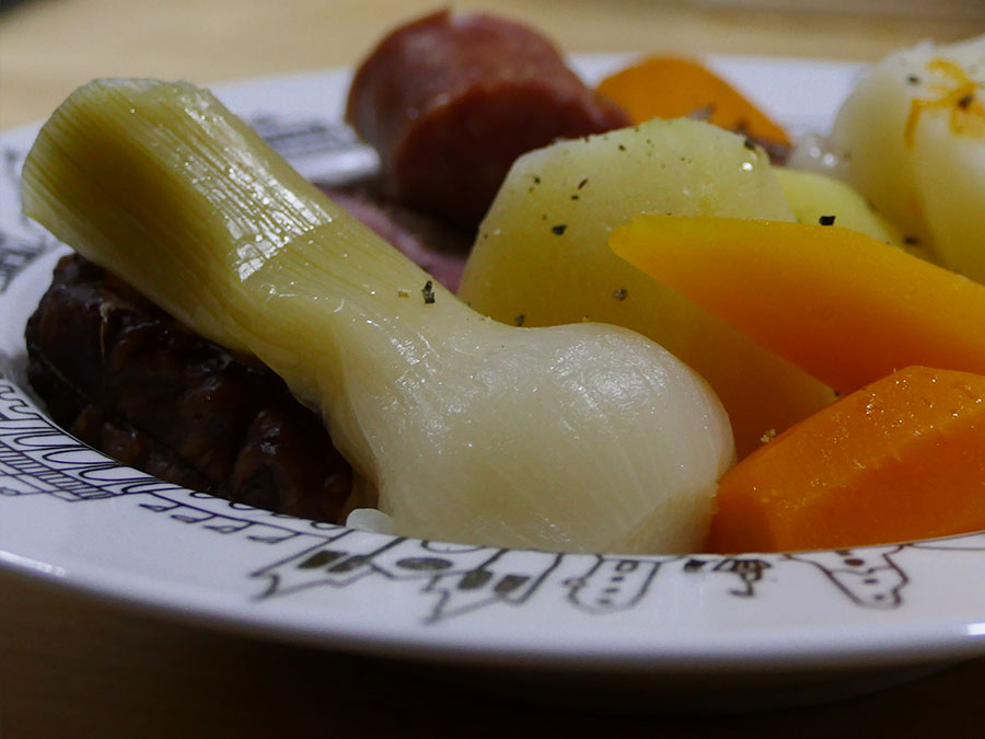 recette de la potée une vrie recette d'hiver avec des carottes multicolores et des patates douces, côté viande, des saucisses fumées, le tout présenté dans une assiette à soupe basque éditée par la manufacture revol, made in france