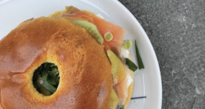 un bagel avec de la truite fumée sur un lit de philadelphia , de l'aillet ciselé, des kiwis jaunes et verts et de l'ail des ours, un bagel de printemps sur une assiette la plage par assiettes et compagnie